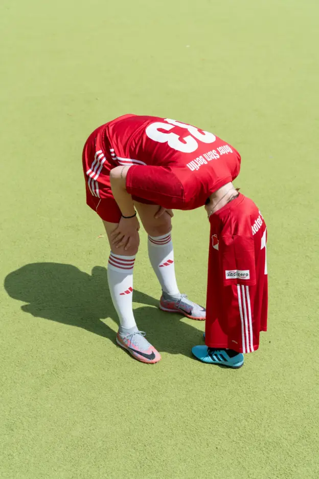 Mensch steht in Fußballkleidung kopüber gebeugt auf einem Fußballplatz.