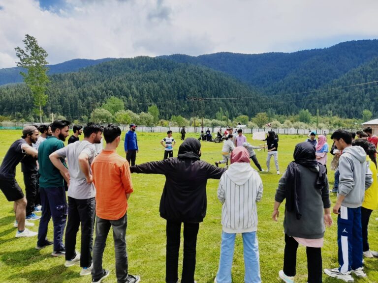 Gruppe junger Menschen steht im Kreis bei einer Trainingseinheit auf einem Sportplatz